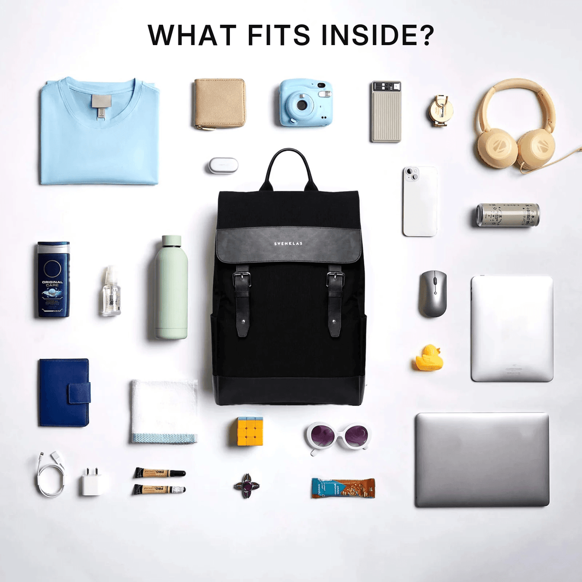 Svenklas Amber black backpack with grey accents is centered in a flat-lay arrangement, surrounded by various everyday items such as a light blue t-shirt, a light blue camera, beige headphones, a white smartphone, a silver laptop, and other accessories. The text 'WHAT FITS INSIDE?' is written at the top.